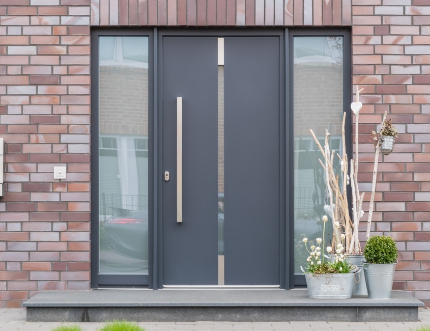 Anthrazitfarbene Aluminium-Haustür mit zwei Glas-Seitenteilen an einer Klinkerfassade
