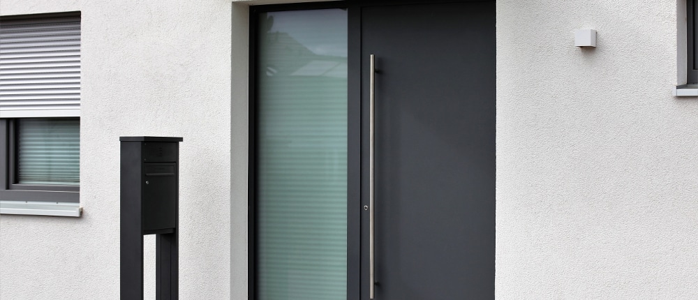 Moderne anthrazitfarbene Aluminium-Haustür mit satiniertem Glasfeld an einem weißen Neubau