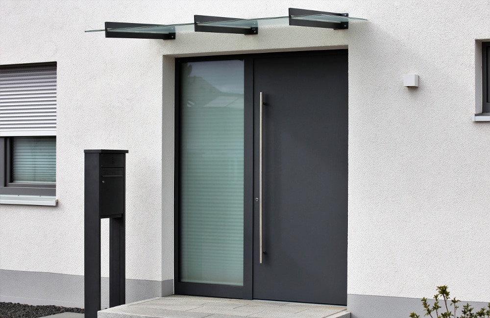 Moderne anthrazitfarbene Aluminium-Haustür mit satiniertem Glasfeld an einem weißen Neubau