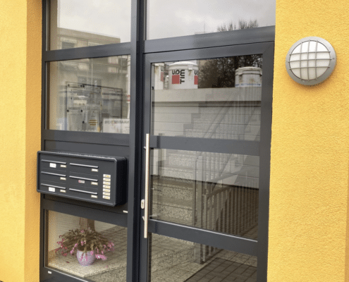 Verglaste Aluminium-Eingangstür für ein Mehrfamilienhaus mit Briefkästen und Klingelanlage