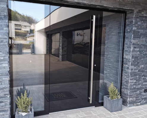 Großflächige Glas-Haustür mit Seitenteil und Edelstahl-Stoßgriff an einer Natursteinfassade