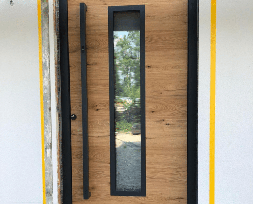 Haustür in Holzoptik mit schwarzem Rahmen, schmalem Glasstreifen und schwarzem Stoßgriff